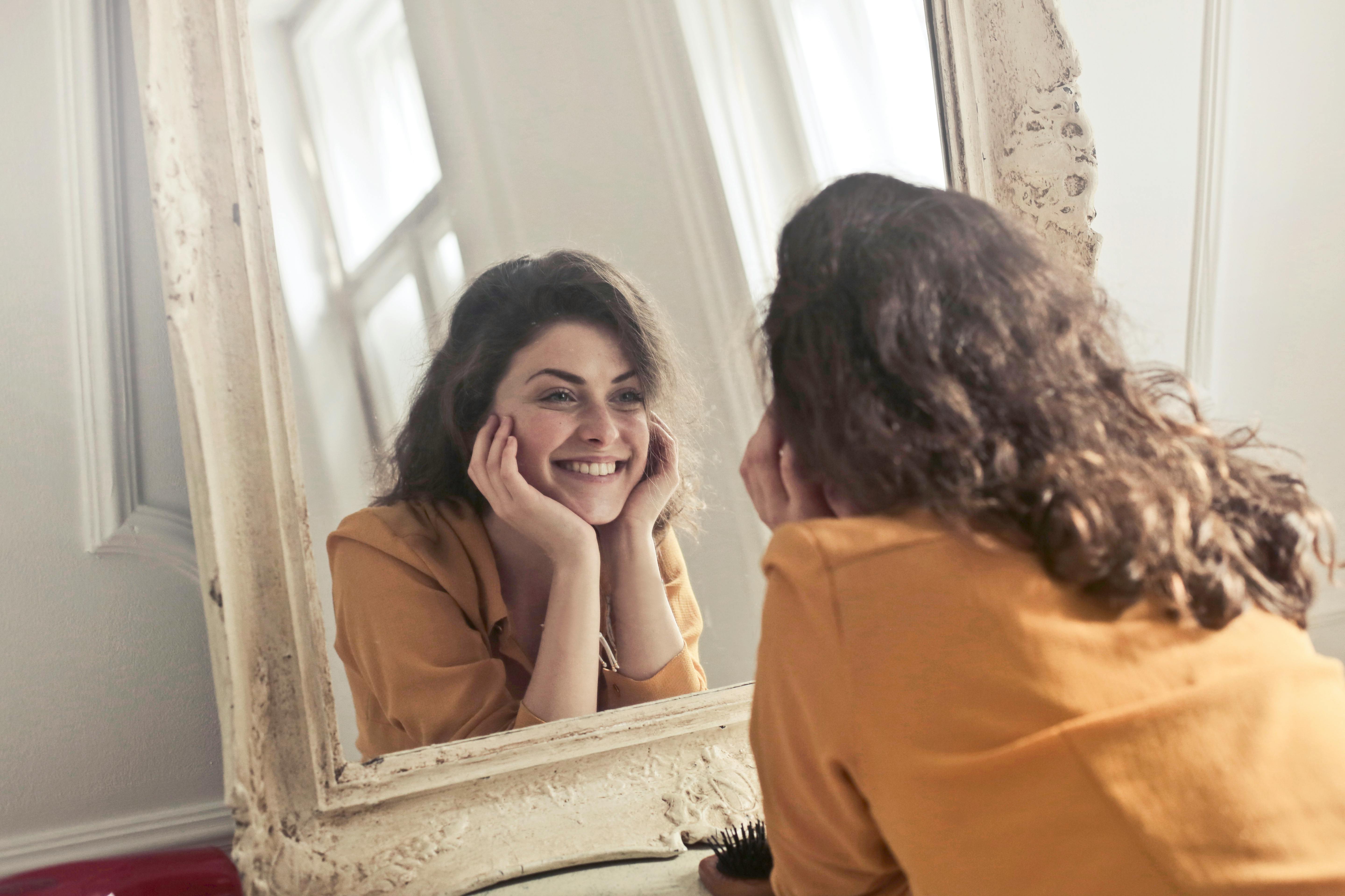 Une femme qui sourit en se regardant dans le miroir.
